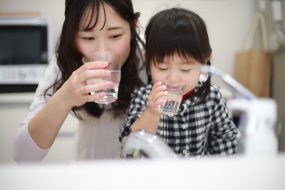Asian mother and daughter drink glasses of water at a stainless steel sink. Asian mother and daughter drink glasses of water at a stainless steel sink,