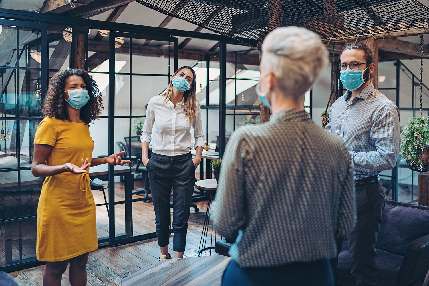Group of entrepreneurs wearing masks and standing at a distance in the office.
