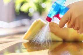 Gloved hand pulls back nozzle on spray cleaner while other gloved hand holds yellow sponge . Gloved hand pulls back nozzle on spray cleaner while other gloved hand holds yellow sponge.