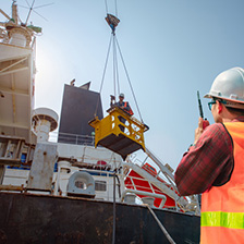 A man with a safety vest and hard hat on talking on a walkie talkie in front of a large ship.