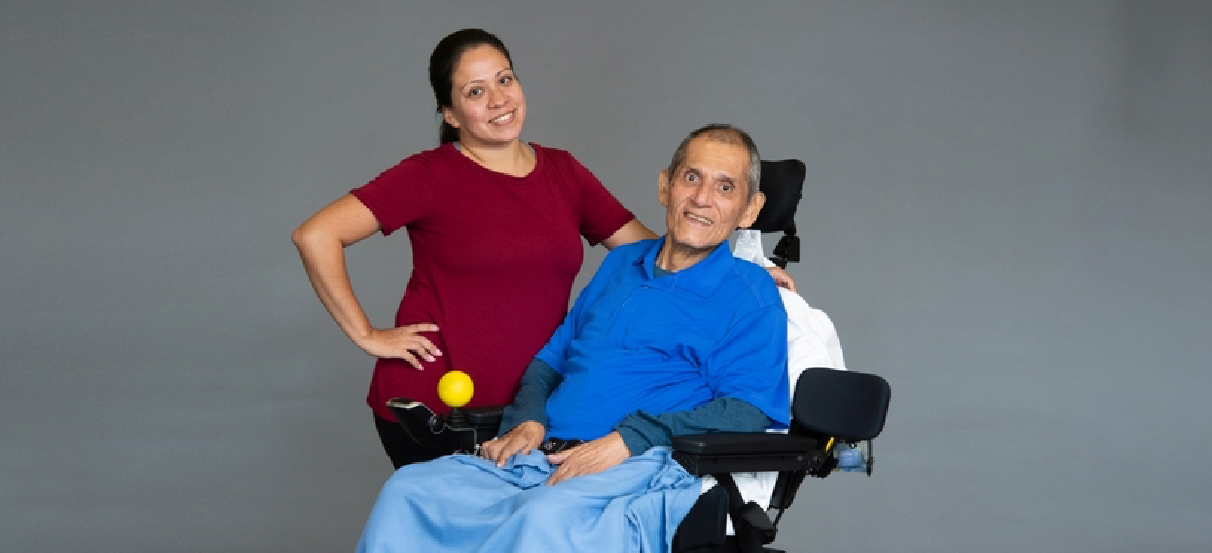 A woman with a red shirt posing with a man in a blue shirt in a wheelchair.