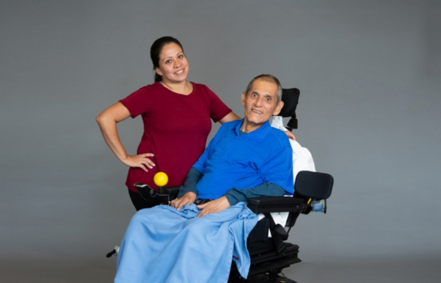 A woman with a red shirt posing with a man in a blue shirt in a wheelchair.