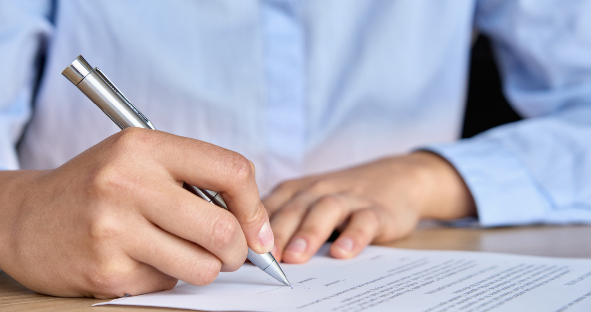 A person wearing a blue shirt is signing a piece of paper using a silver pen.