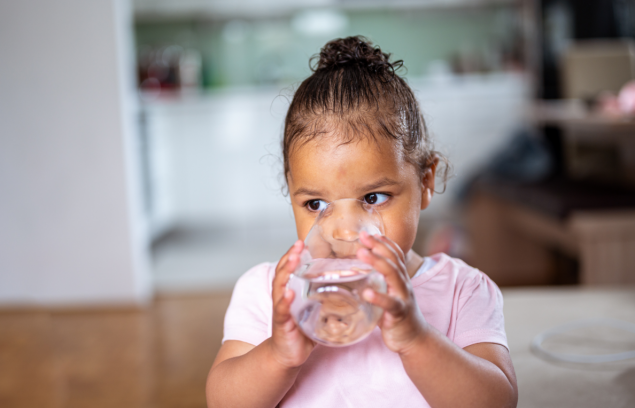 A small child with a pink shirt drinking water out of a glass.