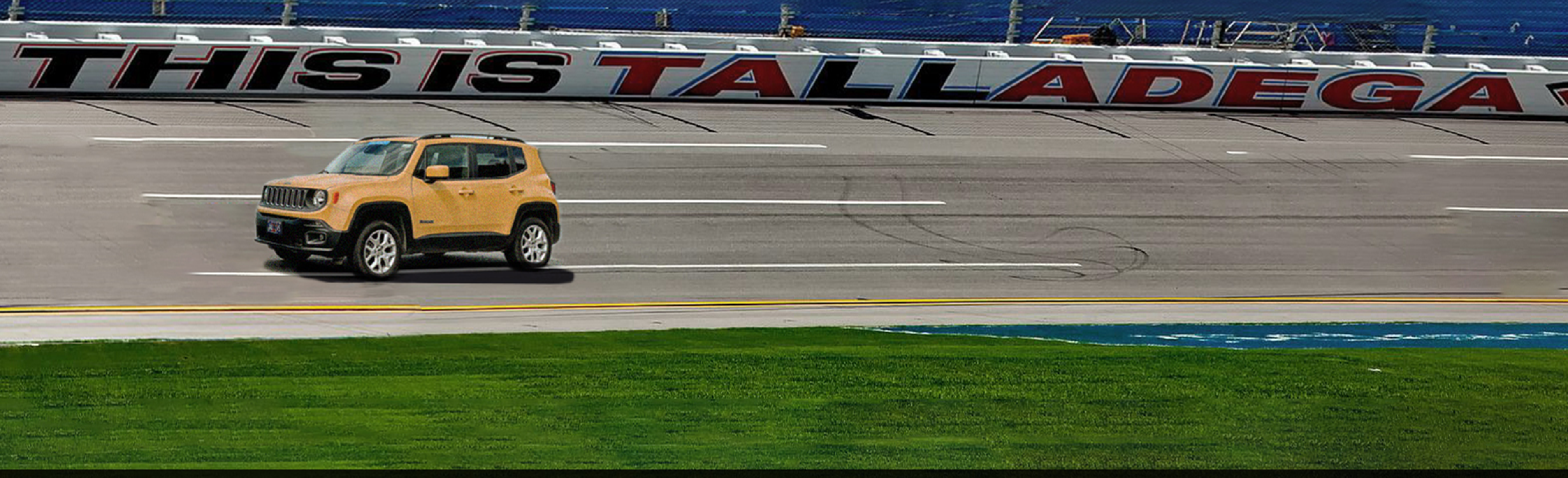 Yellow car driving around the Talladega Superspeedway with “This is Talladega” on a white banner behind it.