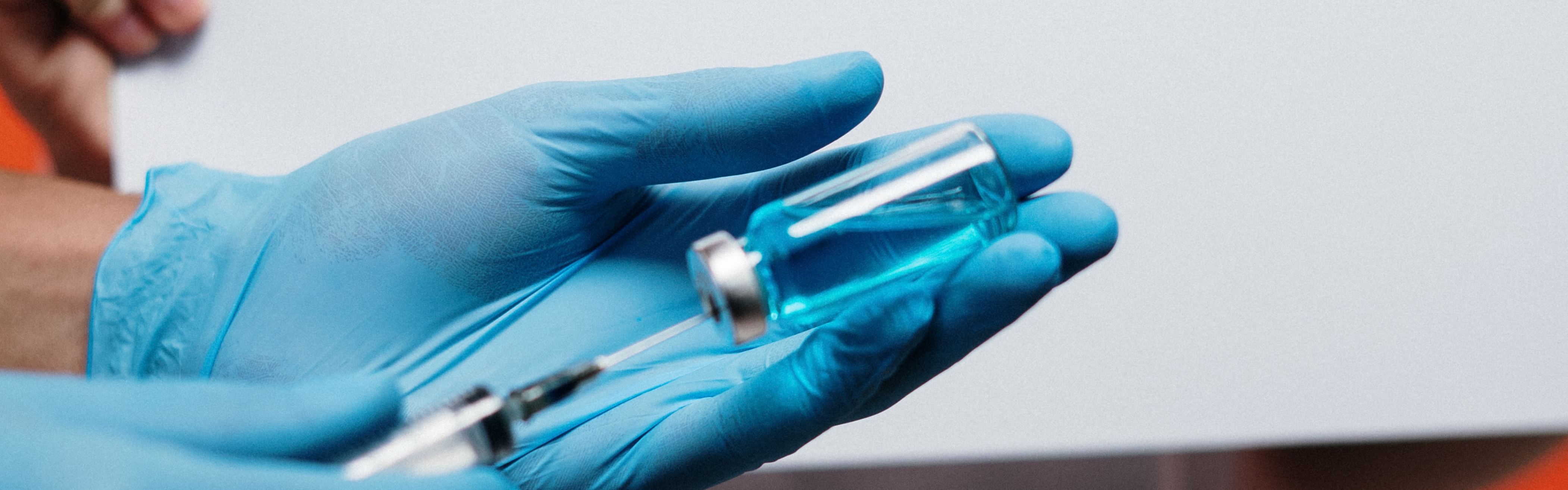 Person’s hands with blue gloves prepare vaccination with a syringe and small bottle.