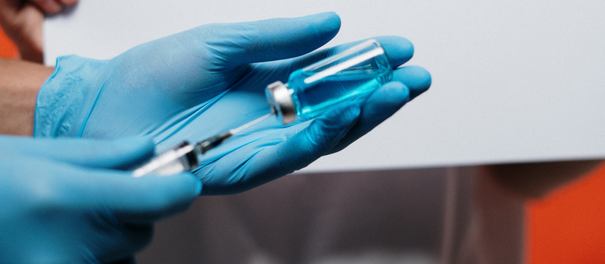 Person’s hands with blue gloves prepare vaccination with a syringe and small bottle.