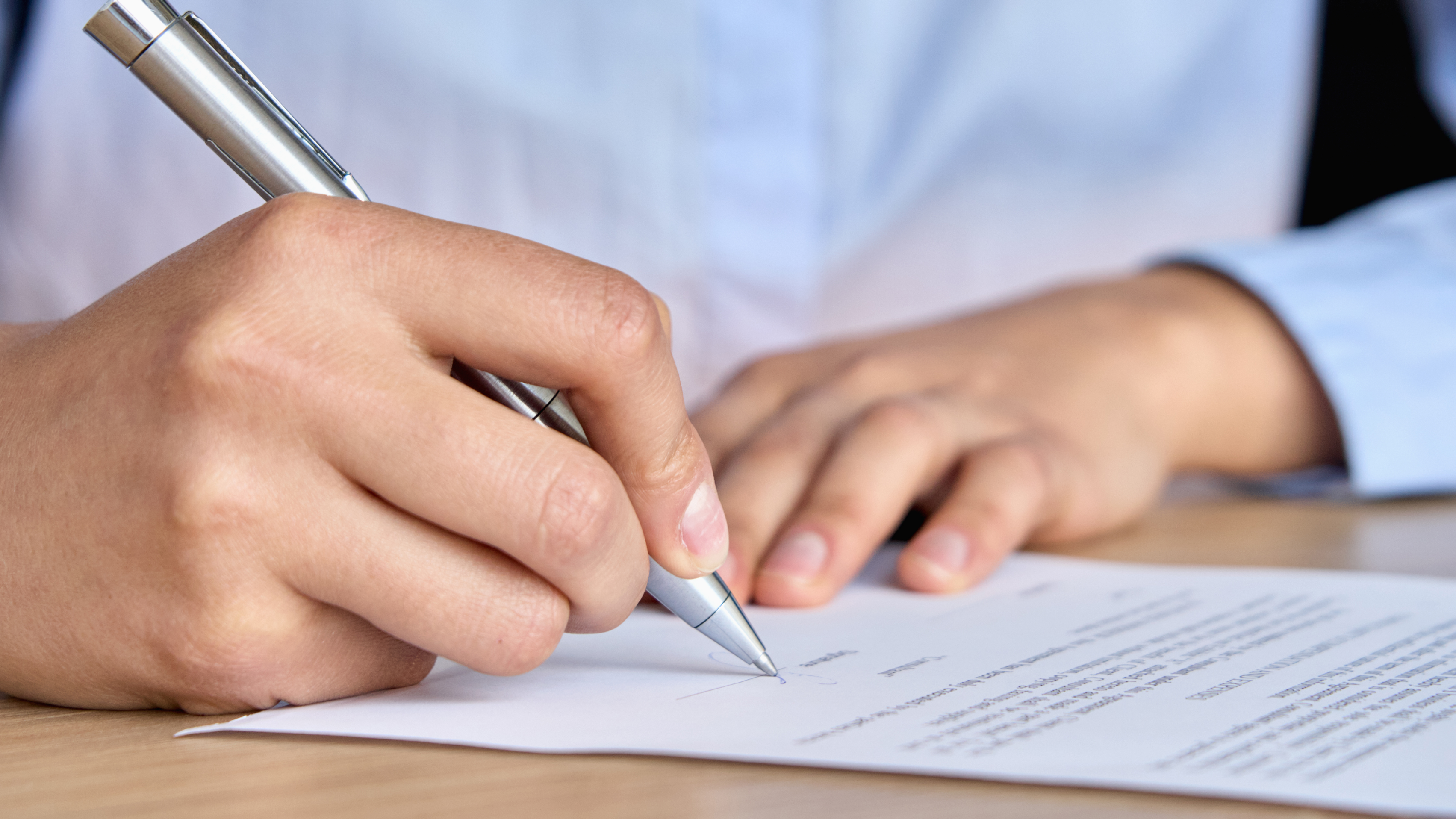 Writing a letter A person wearing a blue shirt is signing a piece of paper with a silver pen.