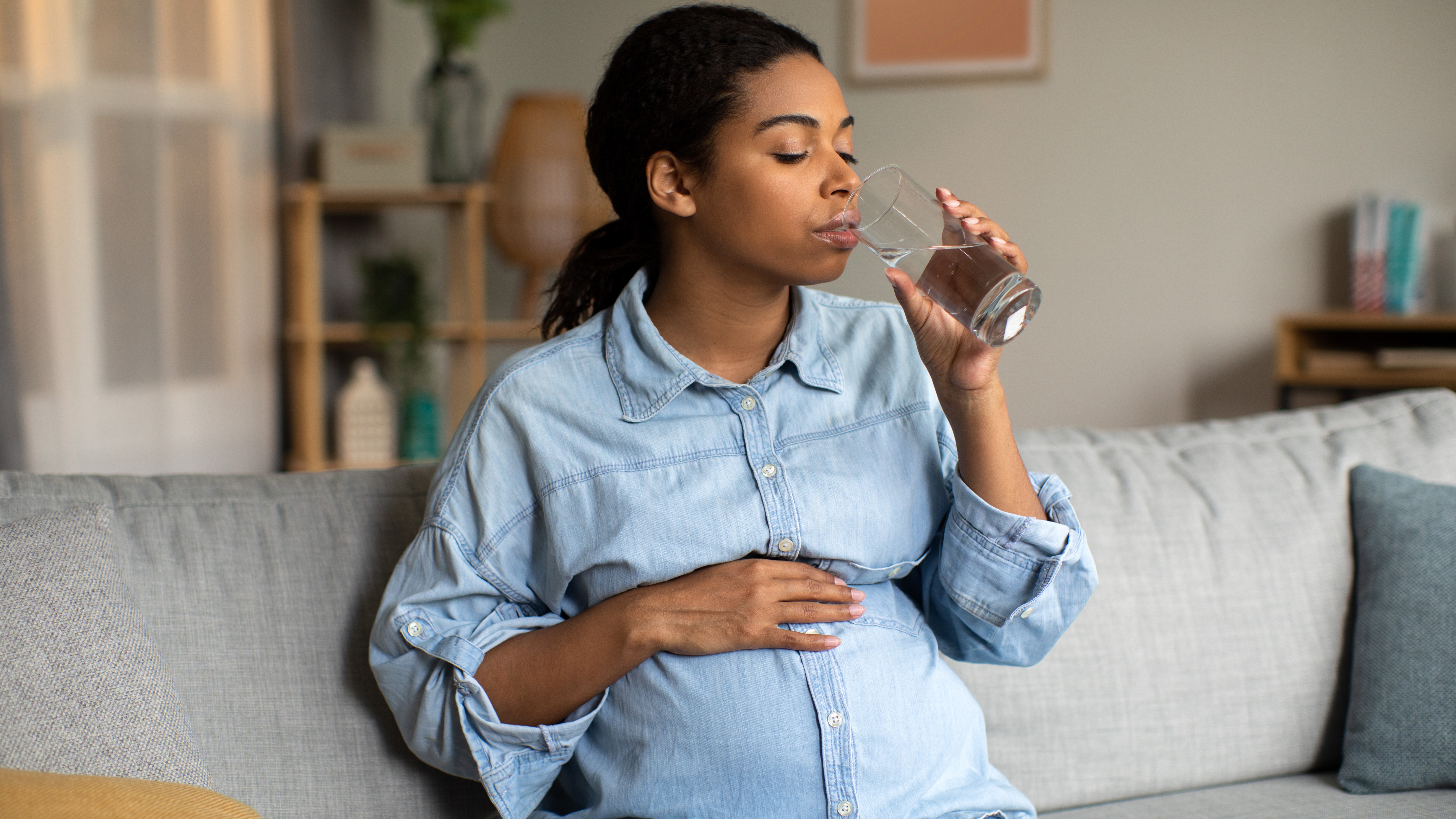 pregnant woman drinking water Pregnant African American lady drinking glass of water at home