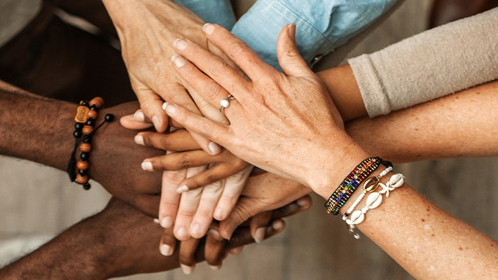Community Engagement Playbook Feature Closed up of a group of diverse people holding hands.