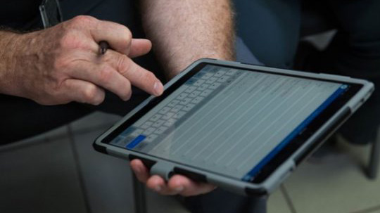CDART App Two hands using an app on a large mobile device. One hand is holding the tablet and the other is tapping the screen.