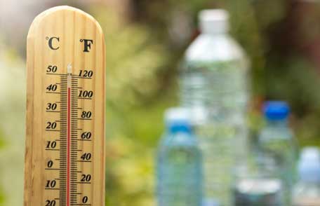 Manténgase fresco cuando hace calor Un termómetro que muestra 110 grados en el suelo con varias botellas de agua detrás.