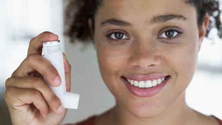 Usted puede controlar el asma Una mujer joven sonriente que sostiene un inhalador