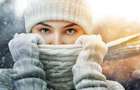 Prepárese para estar sano y seguro en el invierno Una mujer al aire libre con gorro, bufanda, guantes de lana y chaqueta.