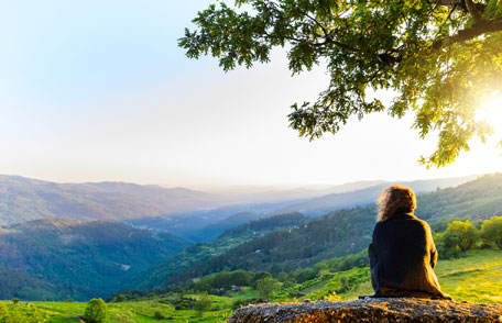 Una mujer sentada en una colina disfrutando de un hermoso paisaje y un cielo despejado y soleado