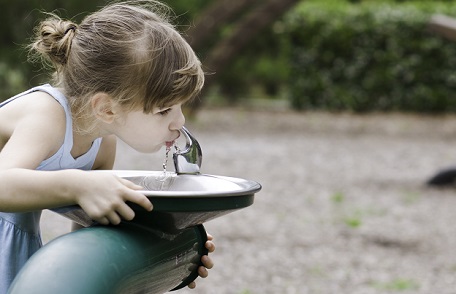 Una niña bebiendo de una fuente de agua pública
