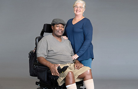 Amyotrophic lateral sclerosis (ALS) patient in a wheelchair smiling with a caregiver.