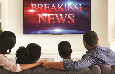 Una familia viendo la televisión. La pantalla del televisor dice Noticias de última hora.