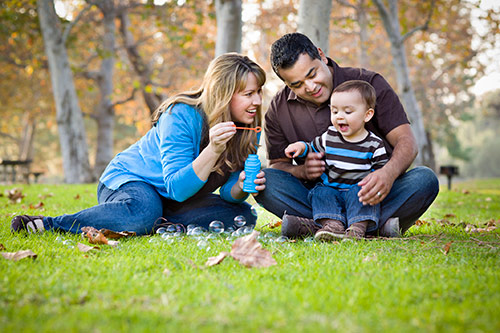 A mother and father play with their young child in the park