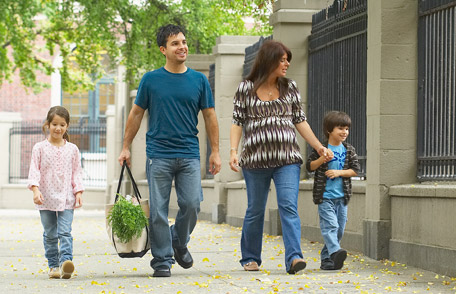 A young couple with children walk down a sidewalk of a city street.