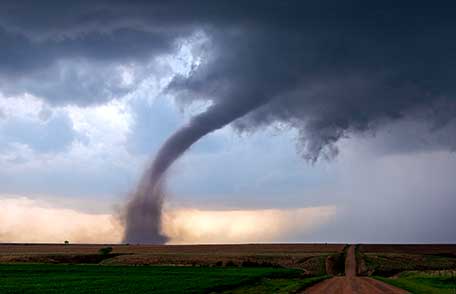 El embudo de un tornado toca el suelo en un campo rural levantando escombros.