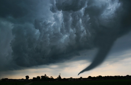 A tornado approaches a town blanketed in dark sky.