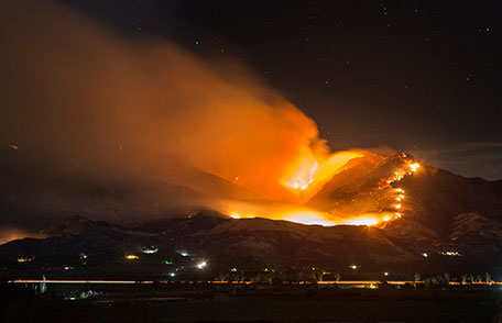 A wildfire rages on the side of a mountain with a town below.