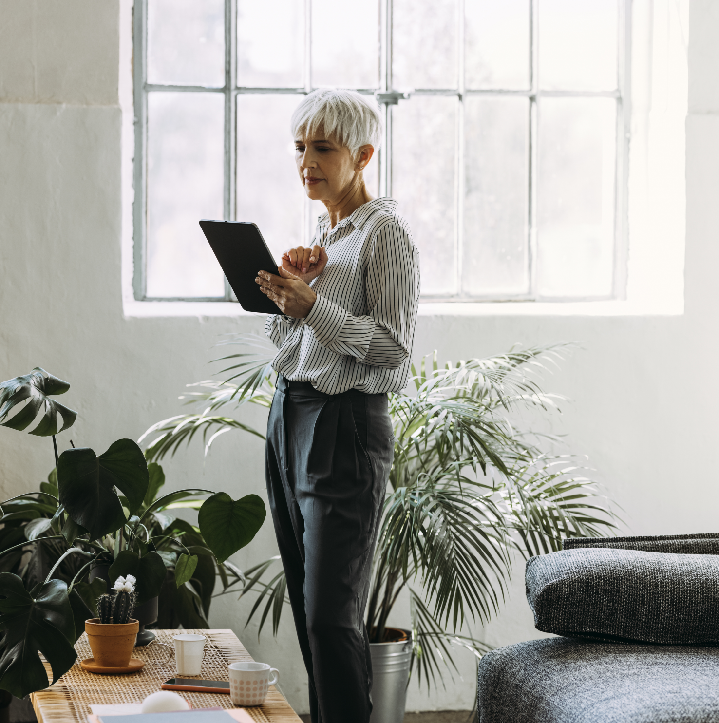 PFAS EA Report A woman with short white hair reading a clipboard with a window and plant in the background.