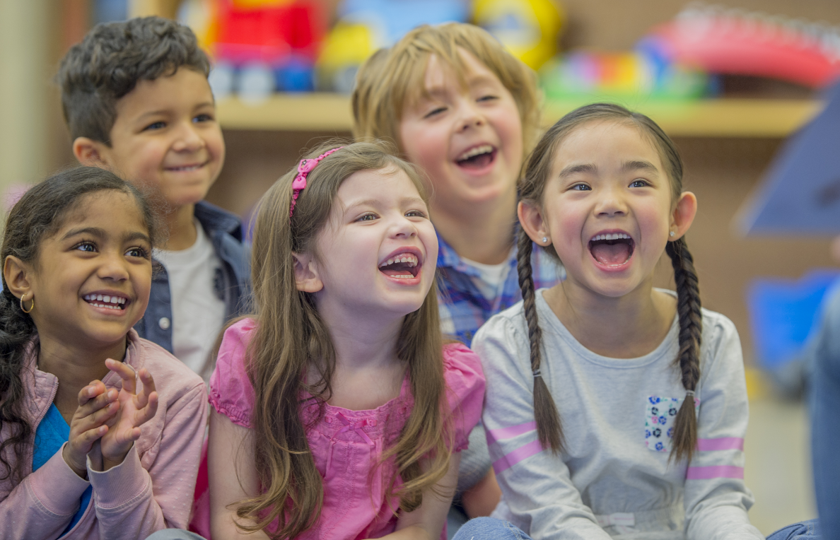 Safe places - landing A group of 5 children sitting down smiling and laughing with colorful books in the background.