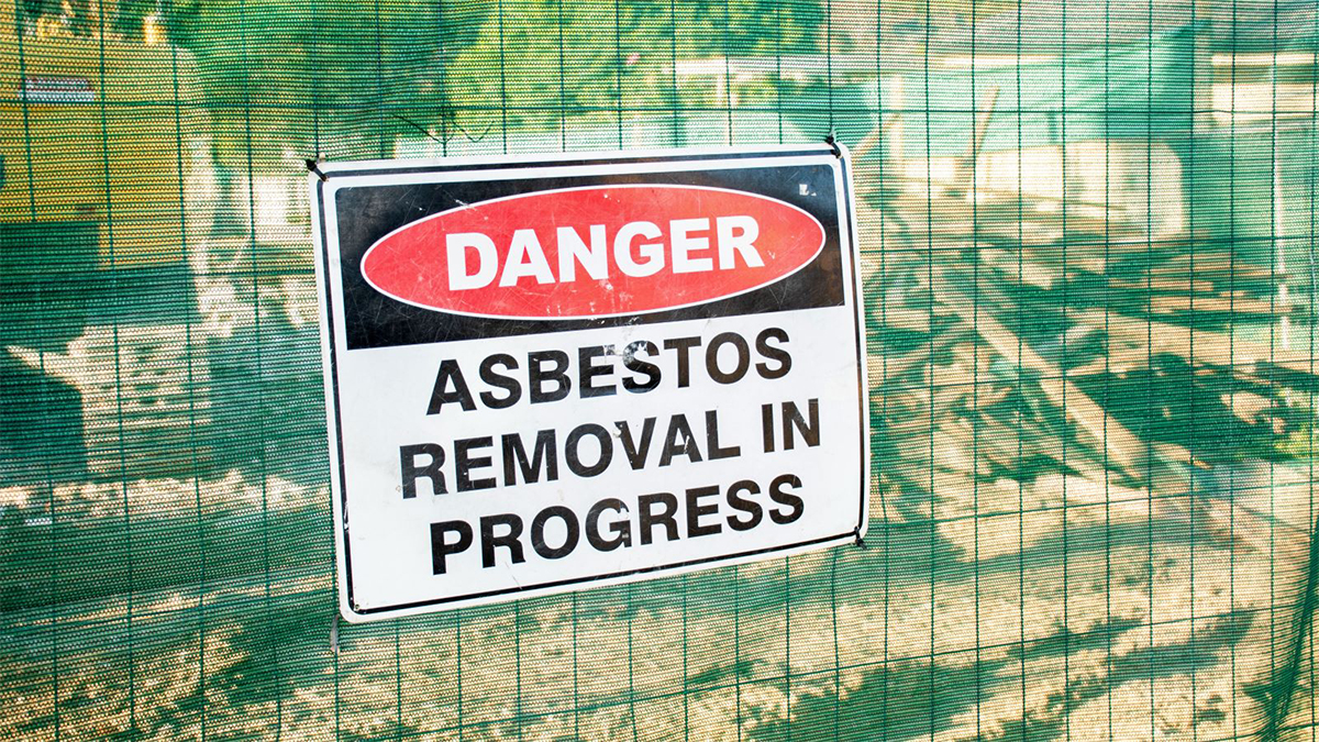 asbestos removal A warning sign Danger Asbestos on a fence at construction site where old house is demolishing
