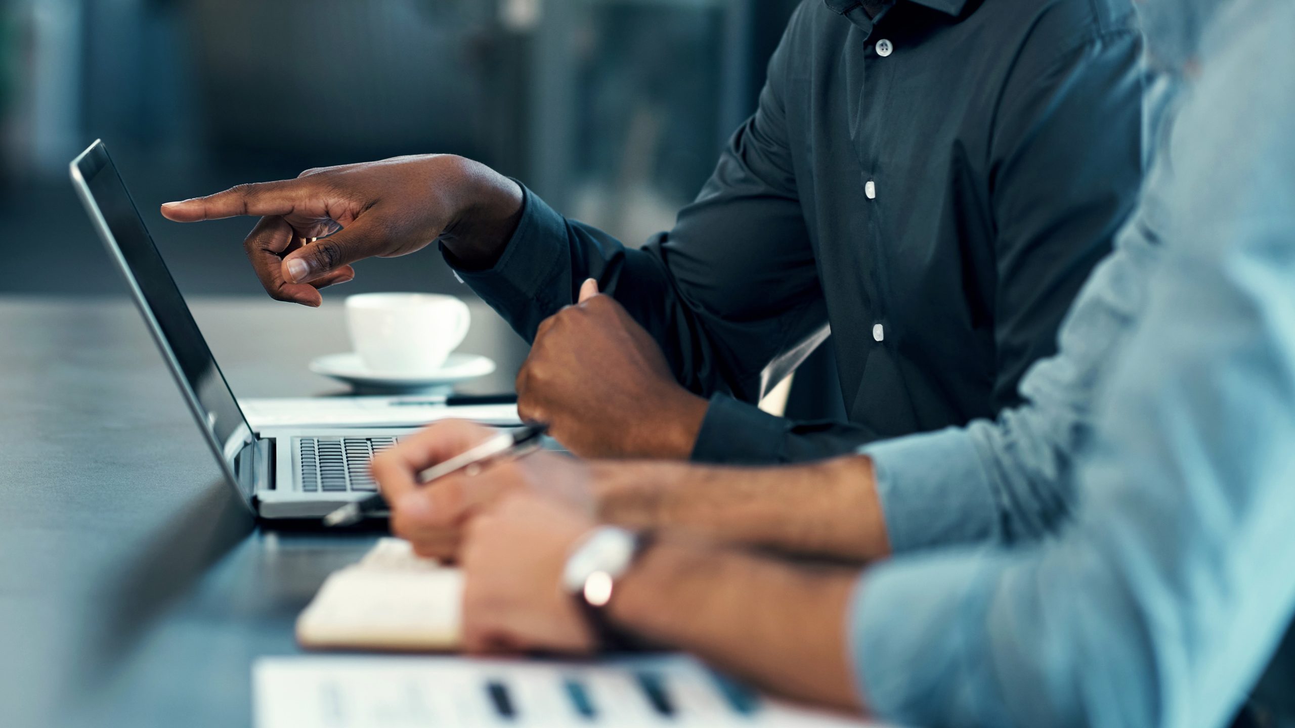 Two people working together with one person pointing at their laptop and another taking notes