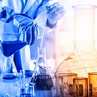 Scientist pouring chemicals from a beaker. Scientist wearing lab coat and gloves pouring a dark blue chemical from one beaker into another. Other beakers sitting on the table containing chemicals, including amber colored beakers.