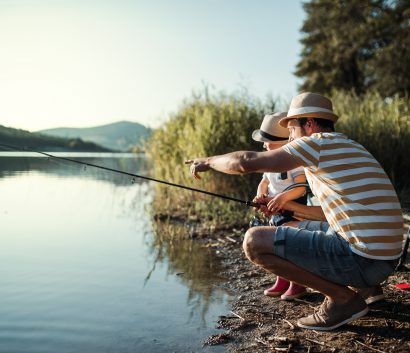 A mature father with a small toddler son outdoors fishing by a lake.