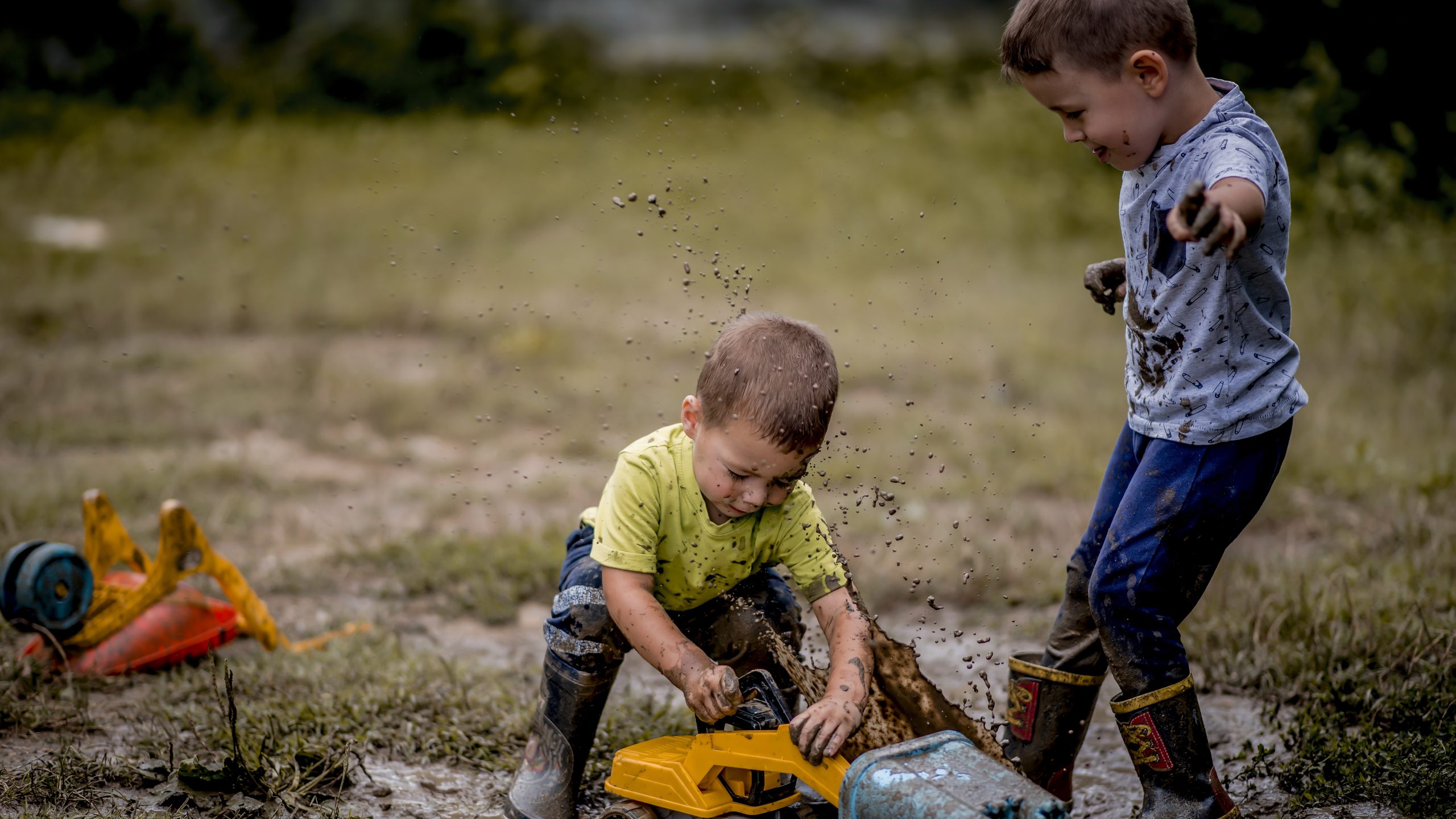 Two young boys playing with toys in the mud