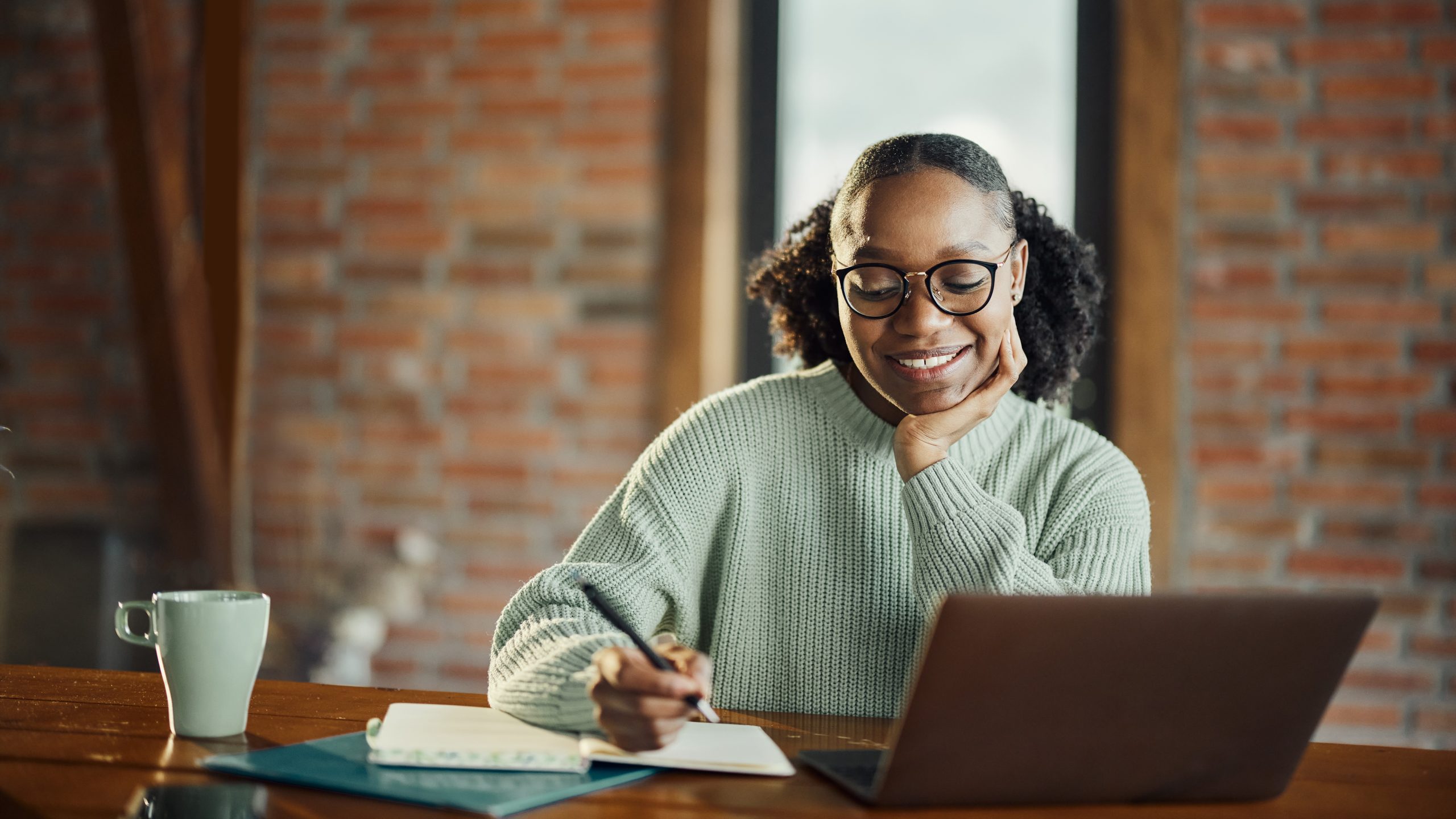 Woman taking notes in front of a laptop.