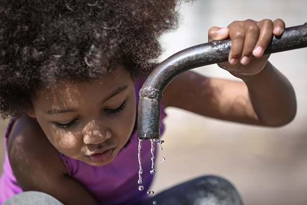 Young girl drinking from a water spout that is dripping water
