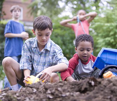 Four children playing in soil with plastic toy truck