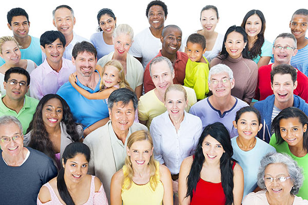 About 30 people smile at the camera, shown from the waist up in a group. Some are children. The group is racially diverse.