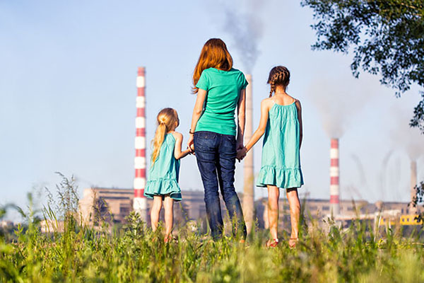 Women holding the hands of two girls starting at factory with smokestacks