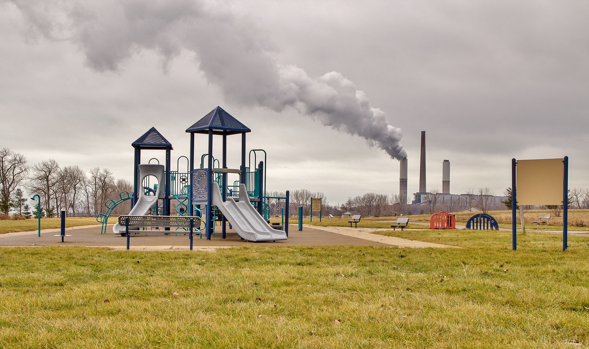 Parque infantil con chimeneas de fábrica liberando contaminación en el fondo