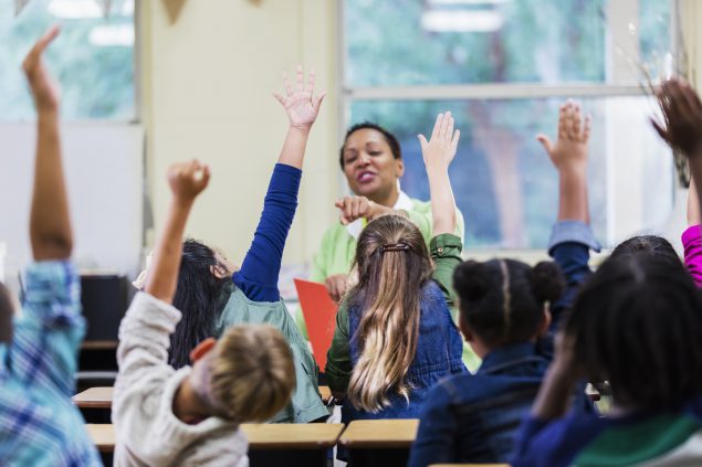 Kids raising hands in a classroom.