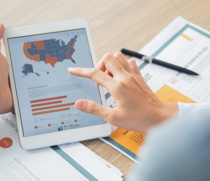 Person at a desk holding a tablet that has a map of the United States and a bar graph.